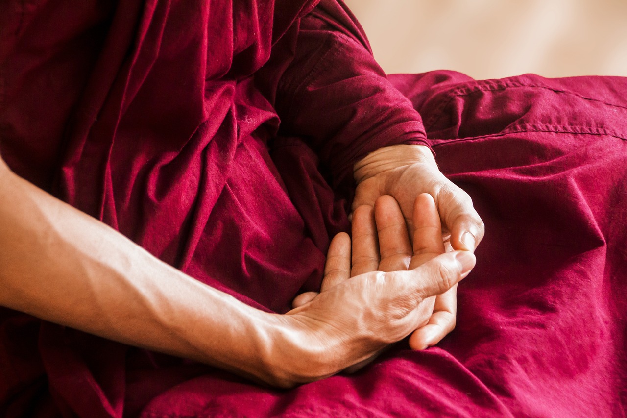 The image shows a close-up of a Buddhist monk's folded hands.